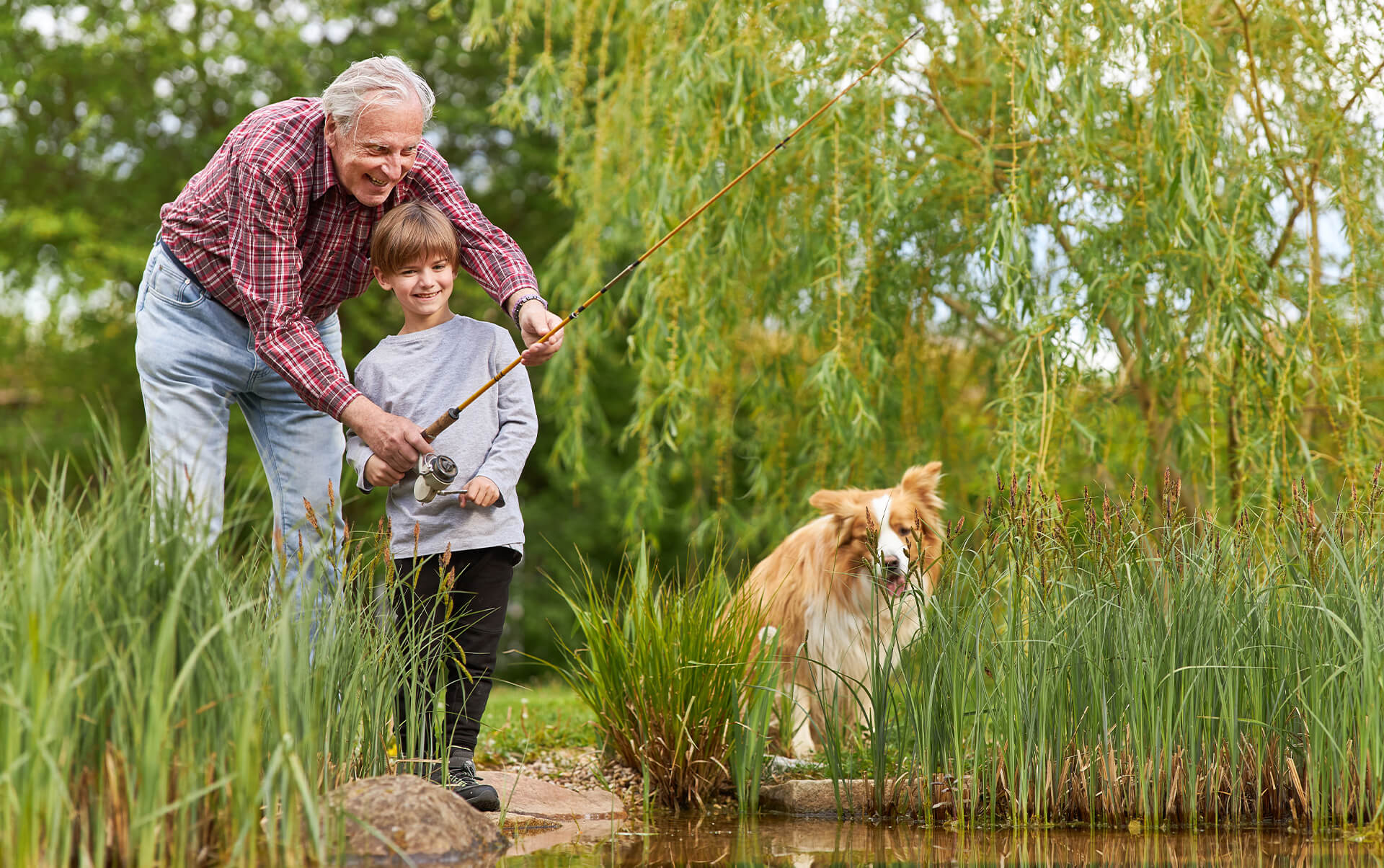 A grandfather teaching his grandson to fish by a pond