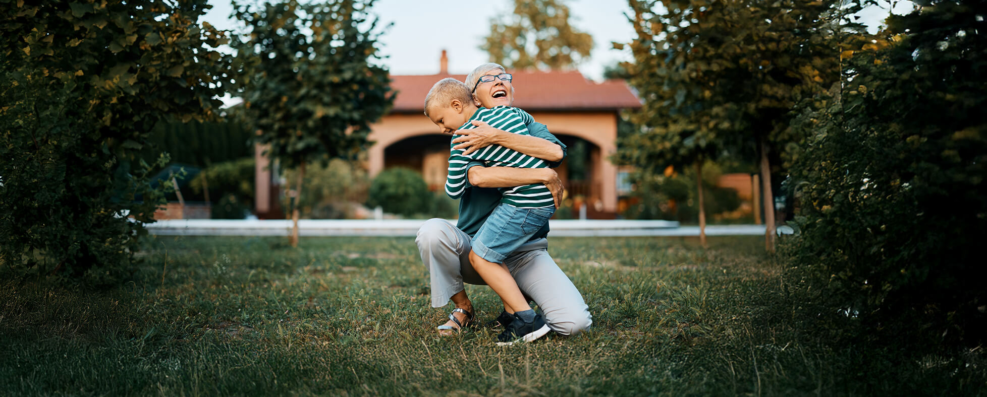 Grandmother laughing as she hugs her grandchild in the backyard