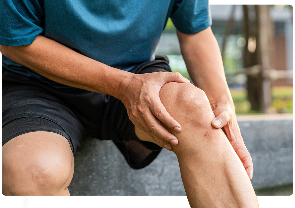 A man sitting outdoors holding his aching knee