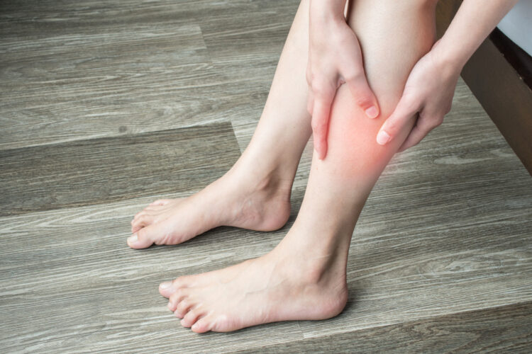 A pair of women's legs with her hands holding a pain point due to blood clots.