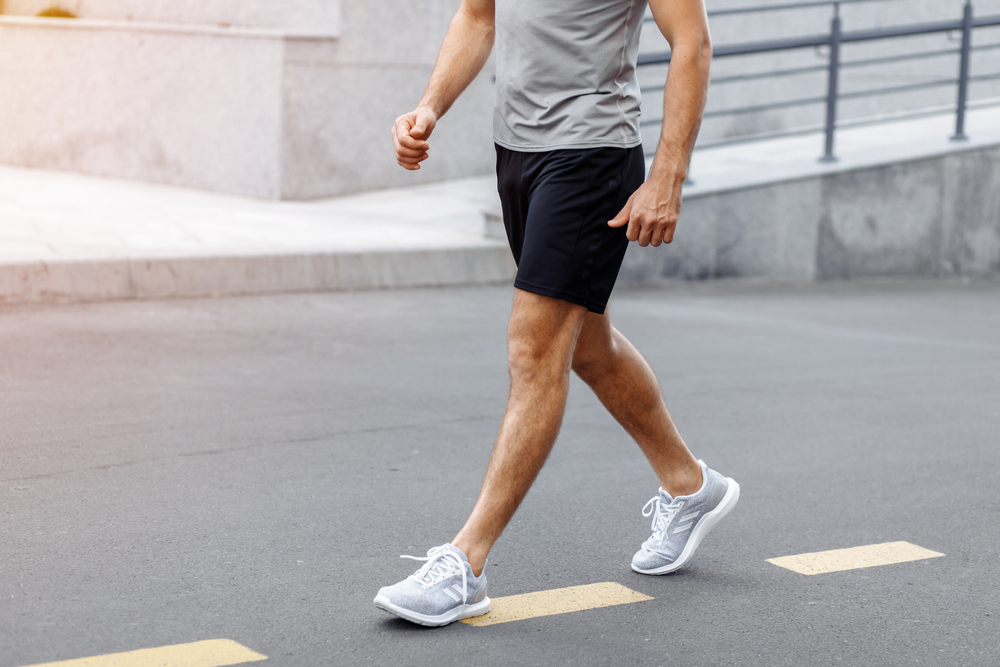 A man walking on a road with the view of the waist down.