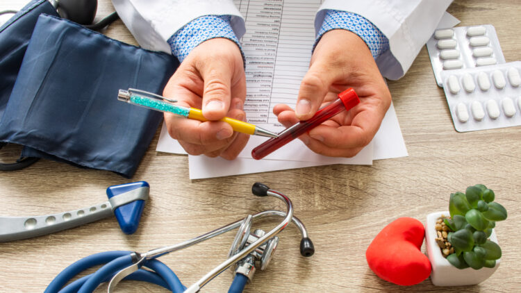 A doctor's hands holding a pen and a vial of blood.