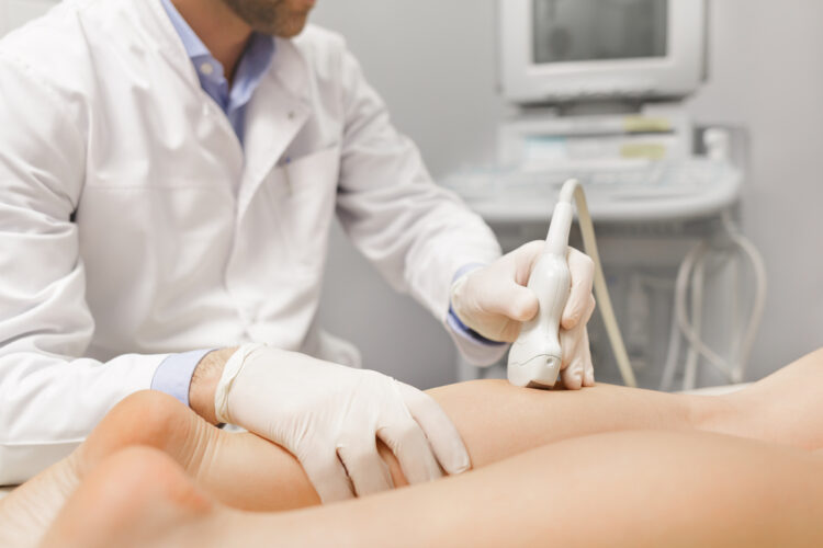 A vascular surgeon using a medical device on a patient with varicose veins.