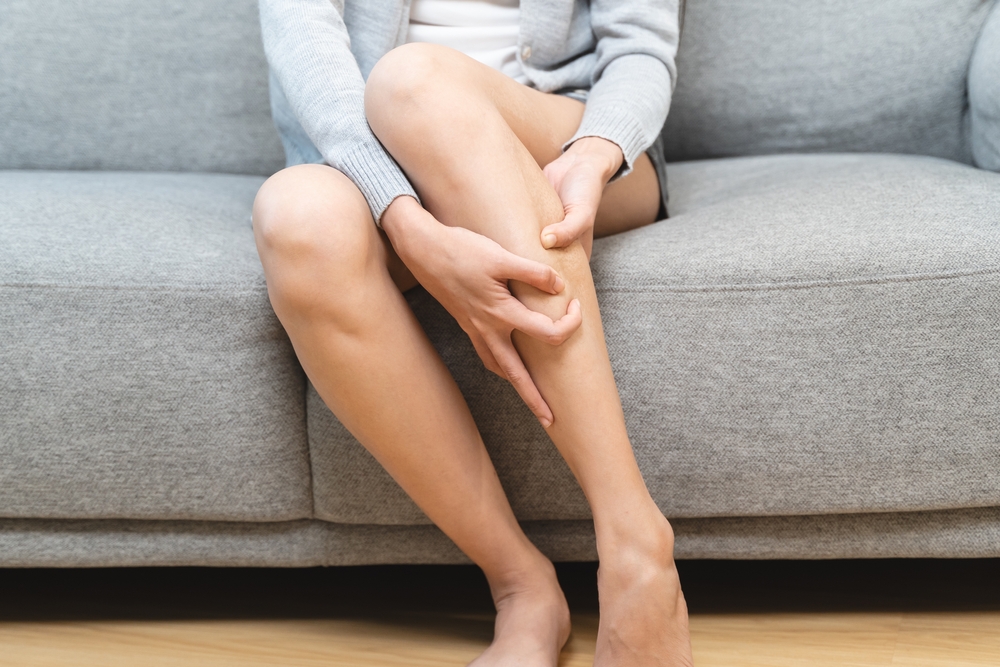 A woman sitting on a couch grabbing her aching leg.